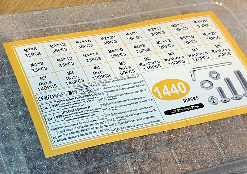 A transparent box of 1440 screws, nuts and washers with a yellow label